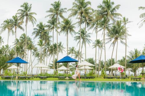 a woman is standing in front of a pool with palm trees at The Blue Water - Geoffrey Bawa Heritage Resort Hotel in Wadduwa