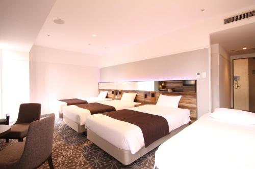 a hotel room with three beds and a desk at Quintessa Hotel Sapporo in Sapporo