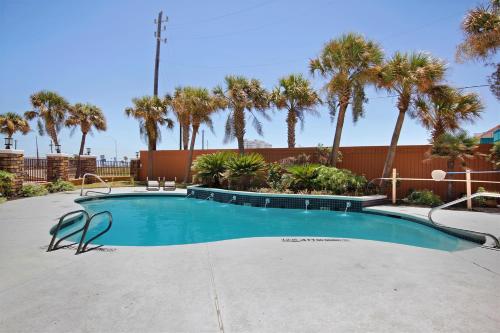 a swimming pool with palm trees and a fence at Best Western Plus Seawall Inn & Suites by the Beach in Galveston