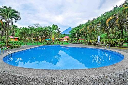 a large blue swimming pool in a resort with palm trees at Hotel Arenal Country Inn in Fortuna