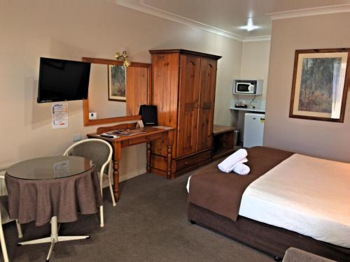 a hotel room with a bedroom with a desk and a bed at New England Motor Inn in Armidale