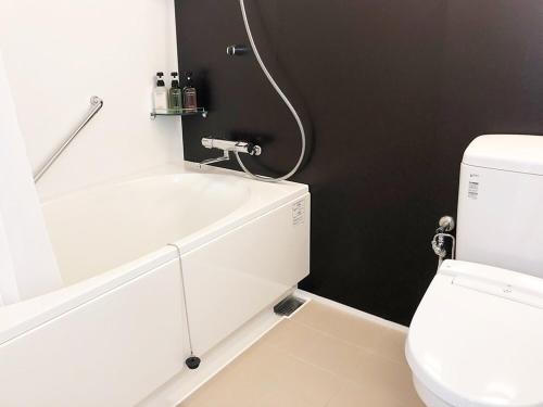a bathroom with a white tub and a toilet at Hotel Sakurano Familia Nago in Nago