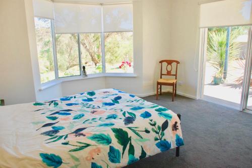 Back Valley Farmstay Bed and Breakfast في فيكتور هاربور: غرفة نوم مع سرير مع لحاف من الزهور ونوافذ