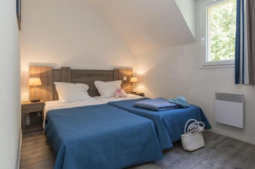 una camera da letto con un letto con una coperta blu e una finestra di Résidence Odalys Domaine de l'Emeraude a Le Tronchet