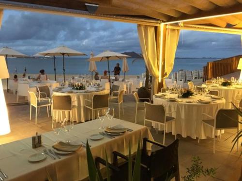 restauracja z białymi stołami i krzesłami oraz oceanem w obiekcie The Ohana Beach Apartment w Corralejo