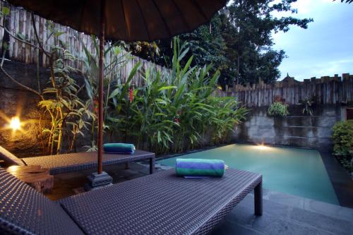 a pool with a table and an umbrella and a bench at The Forest Villa Ubud in Ubud