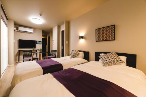 una camera d'albergo con tre letti e una televisione di Trip Base HAKATAEKIMAE a Fukuoka