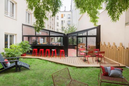 un patio trasero con una terraza con sillas y mesas rojas en Hotel Izzy, en Issy-les-Moulineaux