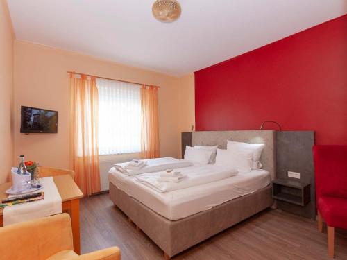 a bedroom with a large bed with a red wall at Hotel Herrlichkeit Dornum Janßen in Dornum