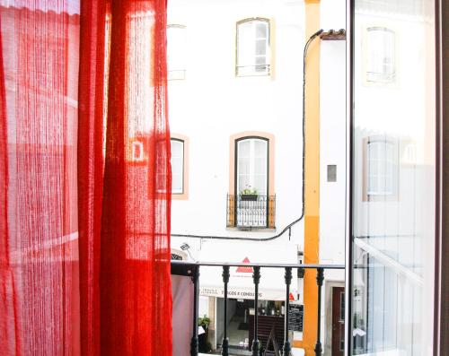 a view of a street from a window with red curtains at Evora Inn in Évora
