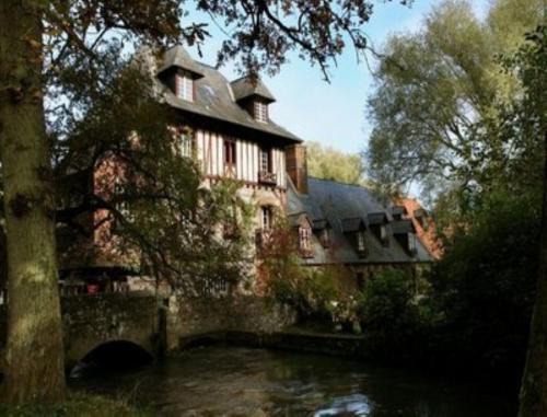 une grande maison avec une rivière en face dans l'établissement Le Moulin Fleuri du Petit Appeville, à Petit-Appeville