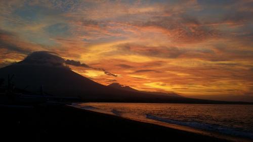 a sunset on the beach with a mountain at De Adema Guesthouse in Amed