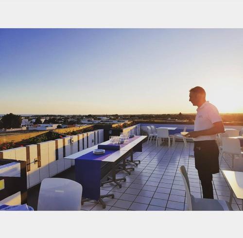 mężczyzna stojący na balkonie ze stołami i krzesłami w obiekcie Hotel Intervallo w mieście Torre Lapillo