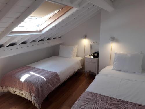 2 camas num quarto branco com uma clarabóia em Casa da Sé em Angra do Heroísmo
