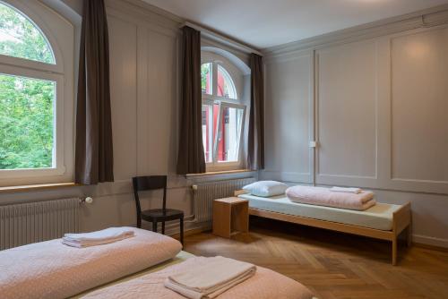 a room with two beds and a chair and two windows at Schaffhausen Youth Hostel in Schaffhausen