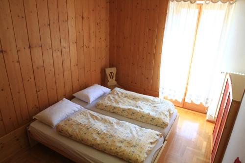 two beds in a room with wooden walls and a window at Casa Elisa in Pozza di Fassa