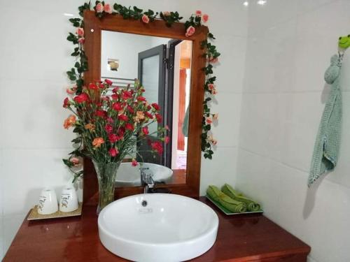 a bathroom with a sink and a mirror and flowers at Phong Nha Rice Field Homestay in Phong Nha
