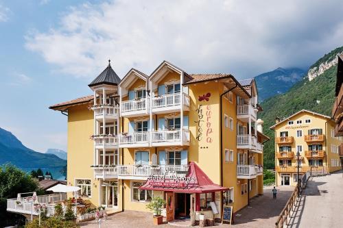 a yellow building with white balconies on a street at Hotel Europa in Molveno