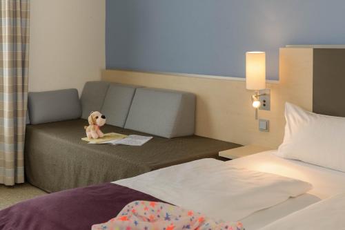 a room with a bed and a teddy bear sitting on a couch at Mercure Hotel Berlin City West in Berlin