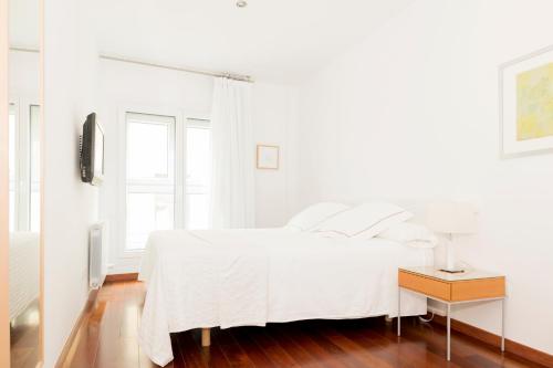 a white bedroom with a white bed and a table at Apartamentos Sabinas El Pilar in Zaragoza