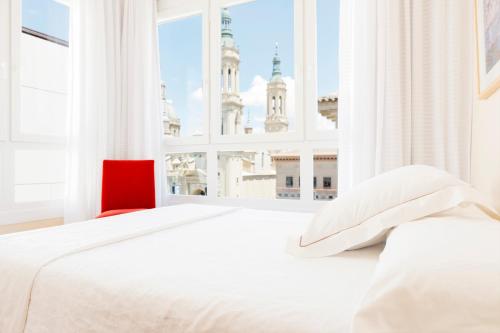 a white bedroom with a red chair and a large window at Apartamentos Sabinas El Pilar in Zaragoza