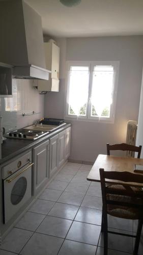- une cuisine avec une cuisinière, une table et des fenêtres dans l'établissement Appartement PAP2S, à Millau