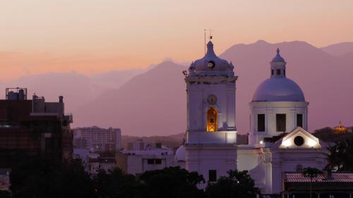a white building with a clock tower with mountains in the background at Hotel Boutique Don Pepe in Santa Marta