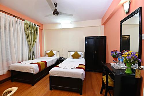 a bedroom with two beds and a desk and a mirror at Hotel Pleasure Home in Kathmandu