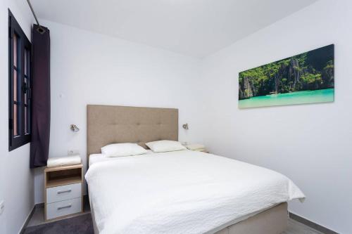 Dormitorio blanco con cama blanca y pintura en la pared en atlantico en Costa Del Silencio