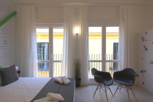 マラガにあるApartamentos Romero Lunaのベッドルーム1室(椅子2脚、ベッド1台付)、バルコニーが備わります。
