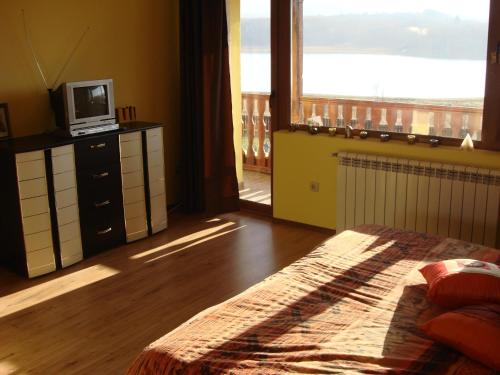 een slaapkamer met een bed, een televisie en een balkon bij Vila on a Lake Lyastoviche Gnezdo near Troyan in Golyema-Zhelyezna