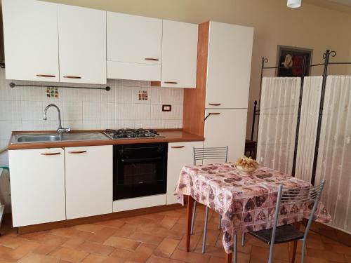 eine Küche mit weißen Schränken, einem Tisch und einem Waschbecken in der Unterkunft La Piccola Toscana 2 in Peccioli