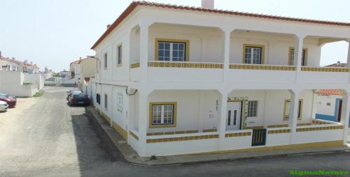 a white building with a car parked in a parking lot at Hostel Nature in Zambujeira do Mar