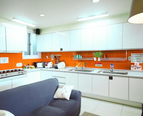 a kitchen with white cabinets and a couch in it at Yeha Guesthouse in Jeju