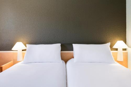 two white beds in a room with two lamps at ibis Nemours in Nemours