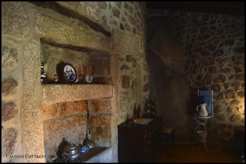 a room with a stone wall with a table and a clock at Castelo Cottages II in Monsanto