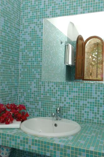 un bagno piastrellato verde con lavandino e specchio di I Dammusi di Borgo Cala Creta a Lampedusa