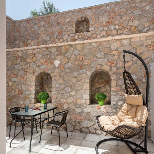 a patio with a chair and a table and a stone wall at Elia Residences Santorini in Karterados