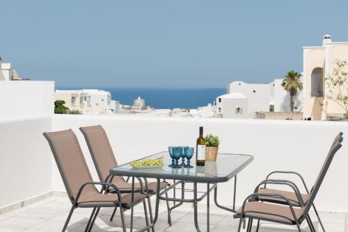 a table with chairs and a bottle of wine on a balcony at Elia Residences Santorini in Karterados