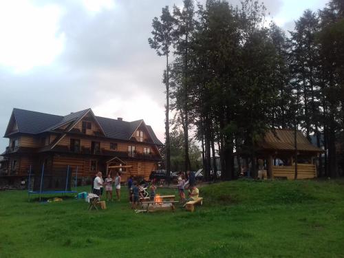 a group of people sitting in the grass in front of a log house at Domek, Apartamenty i pokoje Willa Elita in Kościelisko