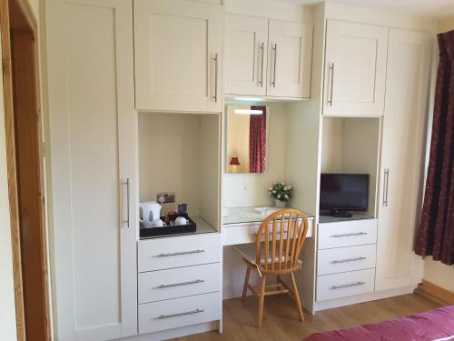 uma cozinha com armários brancos e uma cadeira num quarto em The Three Arches em Louisburgh