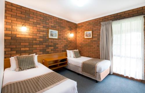 a hotel room with two beds and a brick wall at Sportslander Motor Inn in Moama