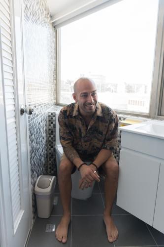 a man sitting on a toilet in a bathroom at May Rooms Taipei Main Station in Taipei