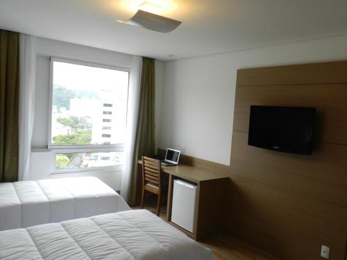 a hotel room with a bed and a desk with a television at Casablanca Center Hotel in Petrópolis