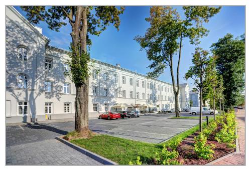 a large white building with cars parked in a parking lot at Koszary Arche Hotel in Góra Kalwaria