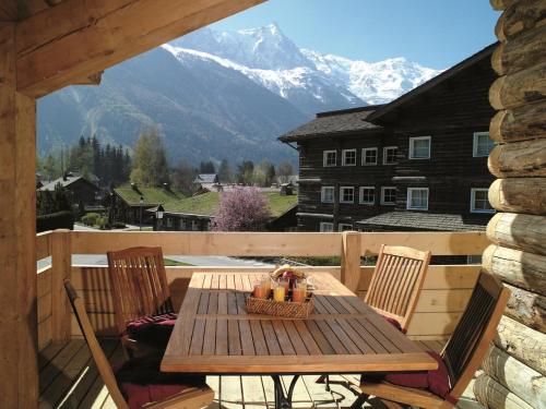 a wooden table and chairs on a deck with mountains at Hôtel Le Labrador in Chamonix-Mont-Blanc