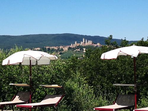 un grupo de sillas y sombrillas con una ciudad al fondo en Castello di Fulignano Ranuccio10 superior apartment, en San Gimignano