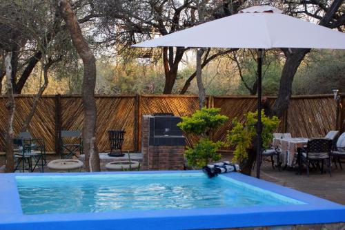 een zwembad met een parasol en een tafel en stoelen bij Marloth Park Hippo House in Marloth Park