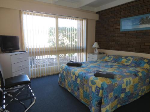a bedroom with a bed and a television and a window at Chapman Court in Merimbula