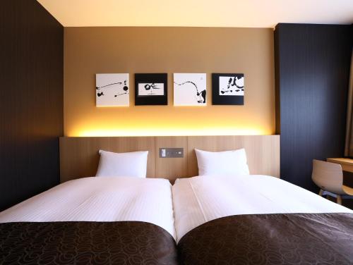 two beds in a room with three pictures on the wall at Hotel Wing International Kyoto - Shijo Karasuma in Kyoto